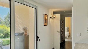 Un pasillo moderno con una puerta corrediza de vidrio que da a un espacio exterior, una pequeña mesa con un florero y un cuadro en la pared.