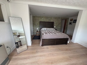 Ein Schlafzimmer mit einem großen Bett, einem Spiegel, einem Nachttisch und einer Lampe.