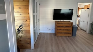 Huoneessa on puulattia, televisio puujalustalla ja avoimen oven kautta näkyy keittiötila.
