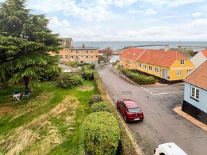 Una strada residenziale con case, un'auto rossa e vista sul mare.