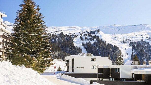 Un bâtiment moderne, sur lequel on peut lire l’inscription « CAPRICORNHE », se dresse au milieu d’un paysage enneigé, avec des montagnes en arrière-plan.