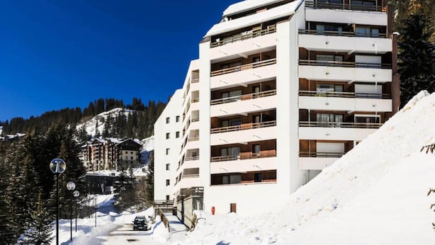 Ett hotell med flera våningar och balkonger, en skidbacke i bakgrunden och en klarblå himmel.
