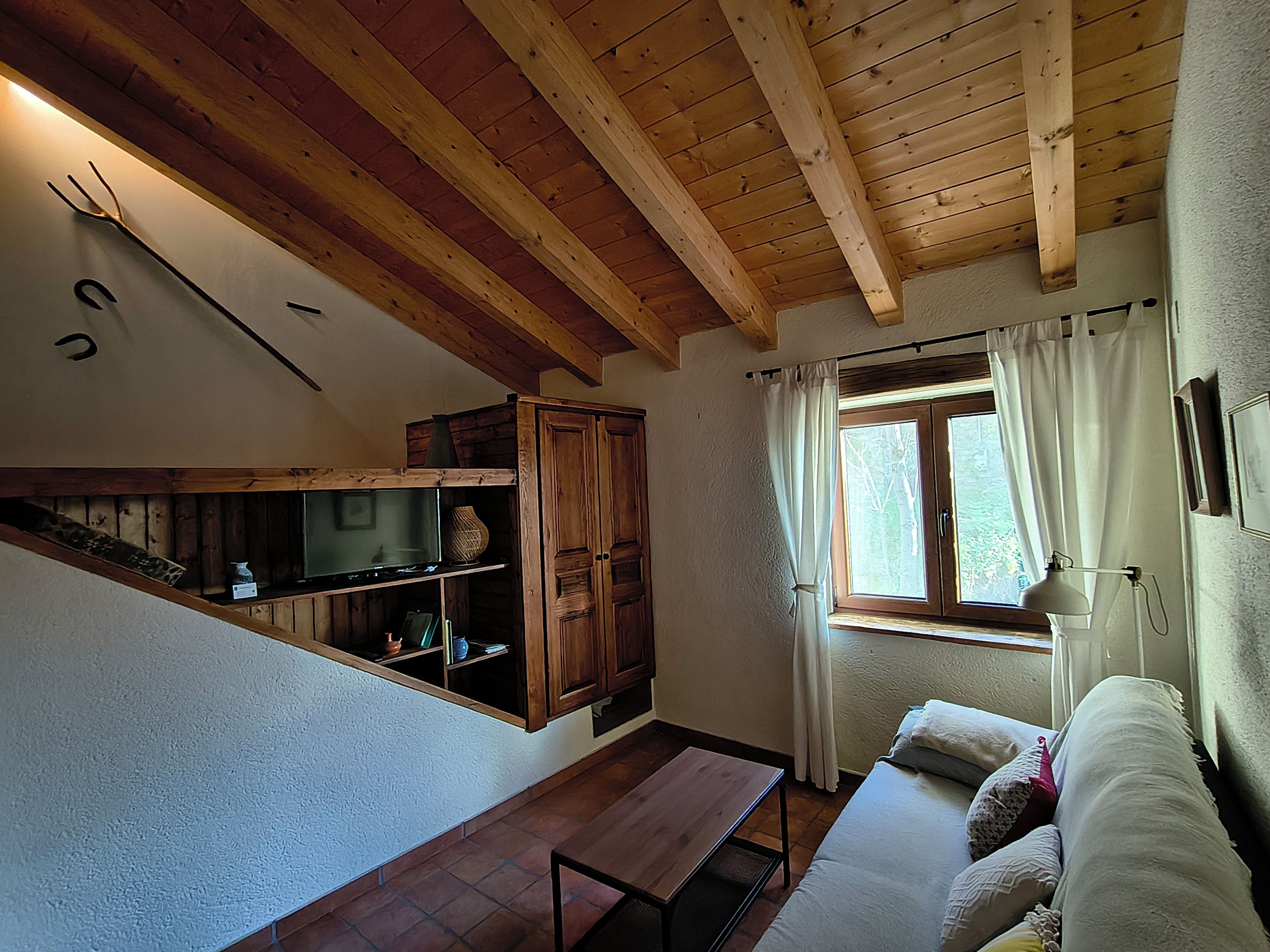 Een kamer met houten plafond, een raam met gordijnen, een bank en een tafel.
