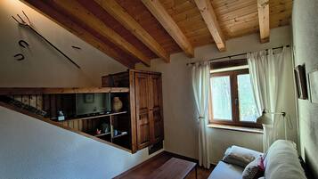 Een kamer met houten plafond, een raam met gordijnen, een bank en een tafel.