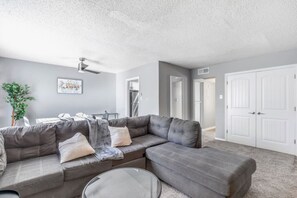 Ein Wohnzimmer mit einer Eckcouch, einem Couchtisch, einem Deckenventilator und einer Tür zu einem anderen Raum.