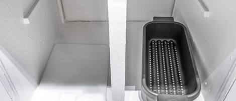 Uno spazio ristretto e chiuso con un contenitore nero forato al centro, probabilmente un cestino, e un pavimento bianco.