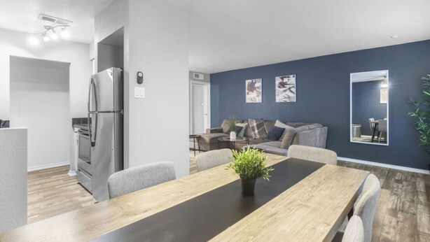 A modern kitchen with a refrigerator, oven, and a dining area with a wooden table and chairs. - Arlington 3BR | AT&T, Globe Life, 6 Flags, Parking (Arlington)