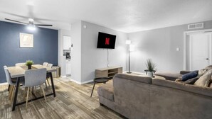 A modern living room with a dining area, a flat-screen TV mounted on the wall, and a ceiling fan. - Arlington 3BR | AT&T, Globe Life, 6 Flags, Parking (Arlington)