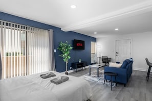 Moderni hotellihuone, jossa on sänky, sininen sohva, työpöytä ja televisio, jossa näkyy Netflix.