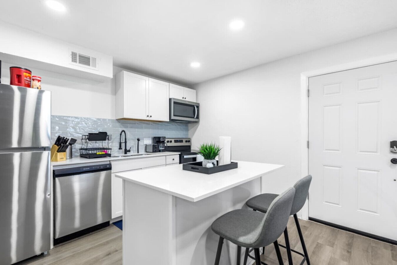 A modern kitchen with stainless steel appliances, white cabinetry, and a small island with bar stools.