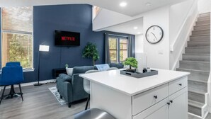 A modern living room with a flat-screen TV, a sofa, a coffee table, and a staircase. - 5 Min to Love Field | Gated+Guard | 2BR | Parking (Dallas)
