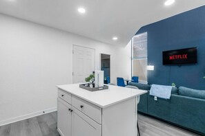 Een moderne woonkamer met een wit kastje, een blauwe bank, een televisie waarop 'NETFLIX' staat en een kleine plant op het kastje.