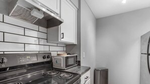 A kitchen with a stove, microwave, and stainless steel trash can. - Arlington 1BR | AT&T, Globe Life, 6 Flags, Parking (Arlington)