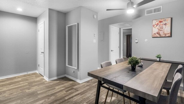 A modern dining area with a wooden table, chairs, a ceiling fan, and a painting on the wall. - Arlington 1BR | AT&T, Globe Life, 6 Flags, Parking (Arlington)
