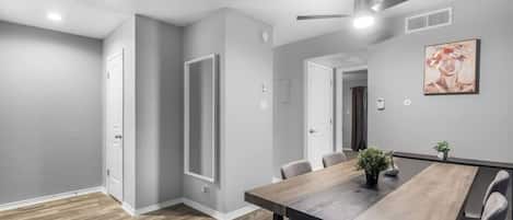 Un comedor moderno con una mesa de madera, sillas, un ventilador de techo y un cuadro en la pared.