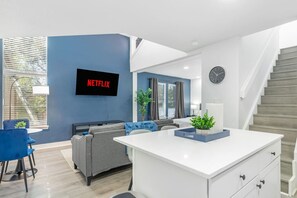 Un apartament modern amb zona de estar, cuina, menjador i escala.