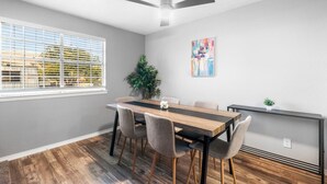 A dining area with a wooden table, four chairs, a ceiling fan, a potted plant, and a painting on the wall. - Arlington 2BR | AT&T, Globe Life, 6 Flags, Parking (Arlington)