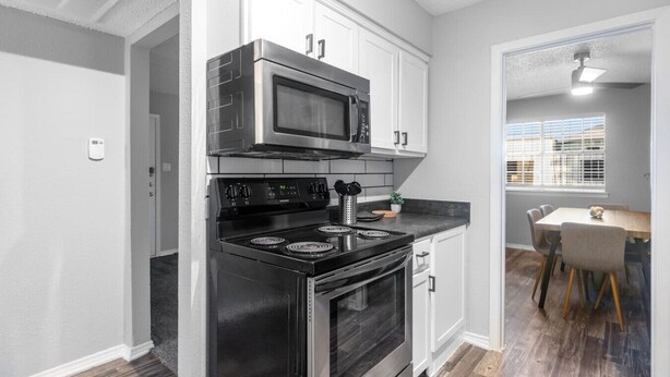A modern kitchen with stainless steel appliances, white cabinetry, and a dining area with a table and chairs. - Arlington 2BR | AT&T, Globe Life, 6 Flags, Parking (Arlington)
