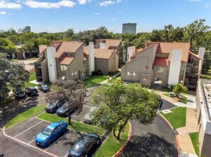 A residential building with a parking lot, trees, and a clear sky. - 5 Min to Love Field | Gated+Guard | 1BR | Parking (Dallas)