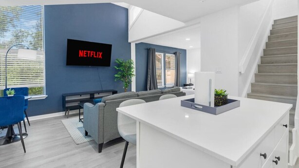 Una sala de estar moderna con televisor de pantalla plana, un sofá, un comedor y una escalera.