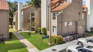 Un edificio residencial con tejado de tejas, césped verde y un estacionamiento con automóviles.