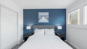 Une chambre à coucher avec un lit, deux tables de chevet avec des lampes, une porte et une fenêtre avec des stores.