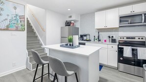 Une cuisine moderne avec des meubles blancs, un four en acier inoxydable et un coin bar équipé de deux tabourets.