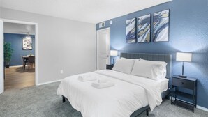 A bedroom with a bed, bedside tables, a door, and a painting on the wall.