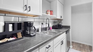 A modern kitchen with white cabinets, a coffee maker, a sink, and a dish rack.