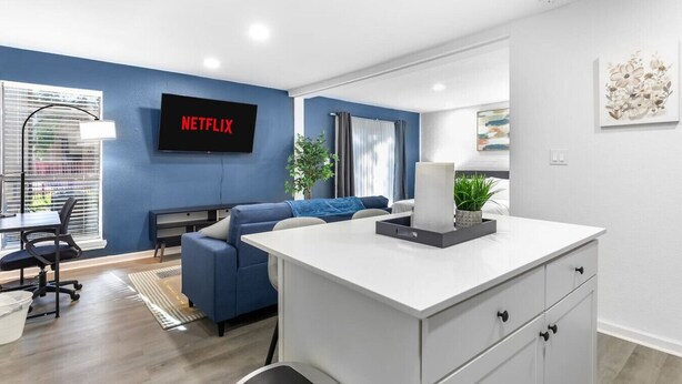 Ein modernes Wohnzimmer mit blauer Akzentwand, einem Flachbildfernseher, einem Sofa, einem Couchtisch und einem Schreibtisch mit Stuhl.