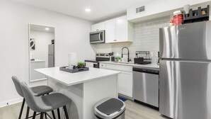 A modern kitchen with white cabinets, stainless steel appliances, and a central island with seating. - 5 Min to Love Field | Gated+Guard | 1BR | Parking (Dallas)