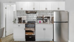 A compact kitchen with white cabinets, a stainless steel refrigerator, a built-in oven, and a gas stove. - Fort Worth Studio3 – 10 Min to Downtown, Gym, Pets (Haltom City)
