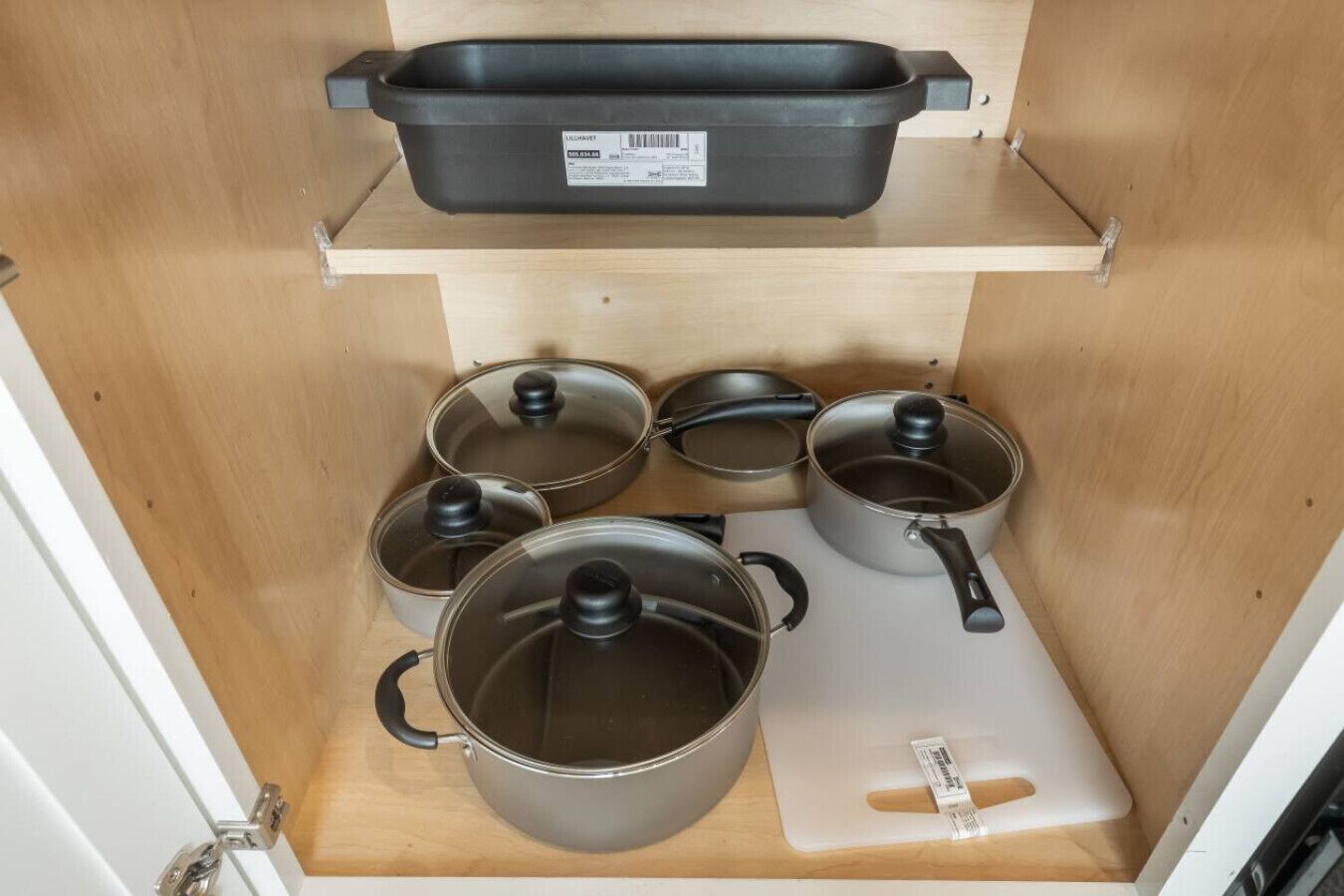 A kitchen with a black baking dish on a shelf, four pots with lids, and a cutting board on the counter.