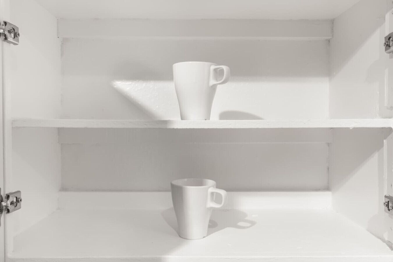 A white shelf unit with two white mugs, one on each shelf.