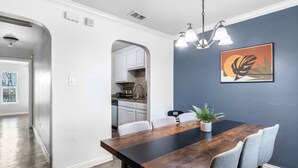 Un área de comedor con una mesa de madera, sillas grises, una planta en maceta y una lámpara fijada a la pared.