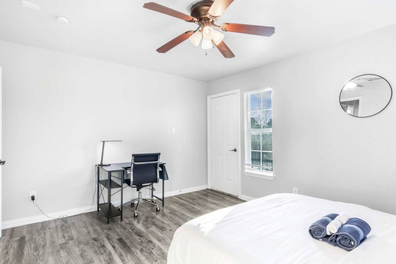 Un dormitorio con cama, escritorio, silla, ventilador de techo, puerta y ventana.