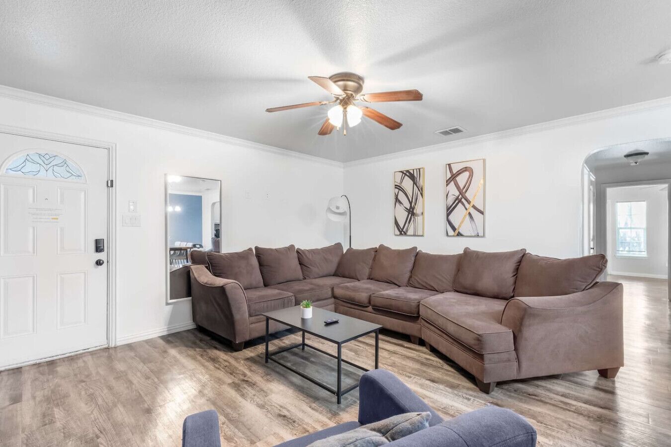 A living room with a sectional sofa, a coffee table, a ceiling fan, and artwork on the walls.