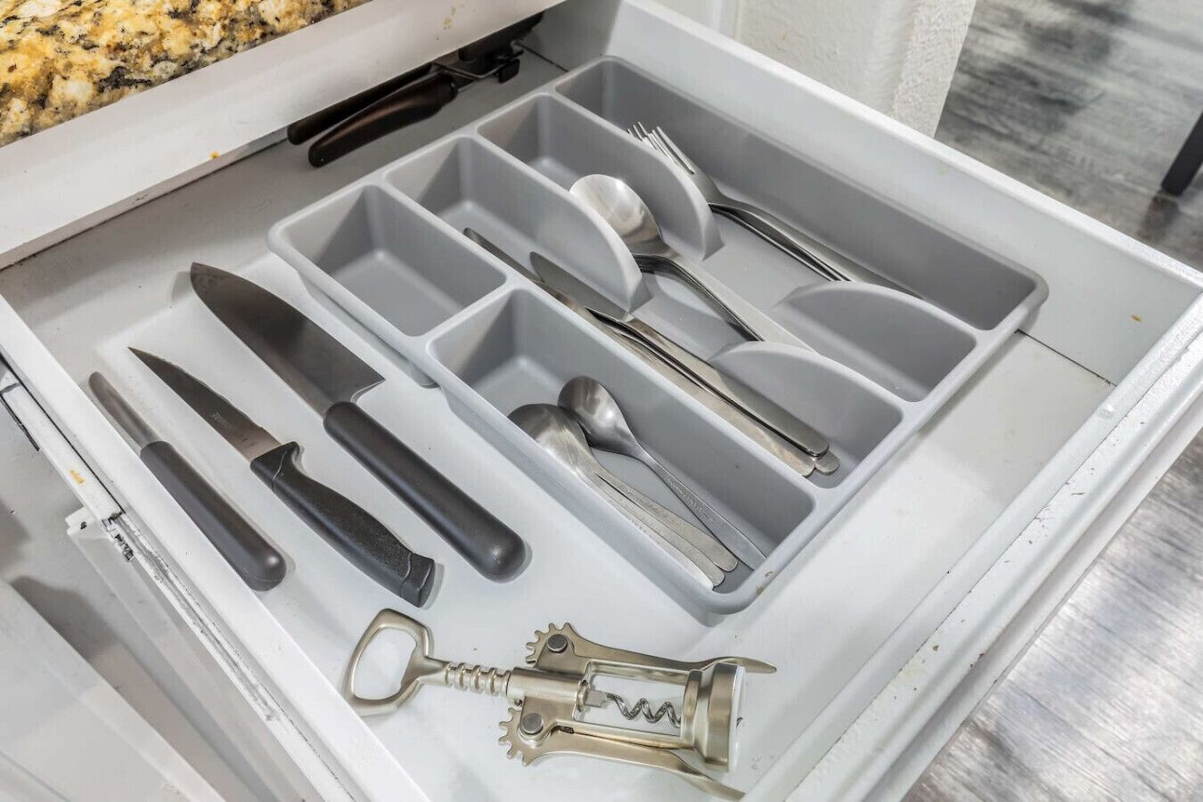 A drawer with compartments containing various utensils and a bottle opener.