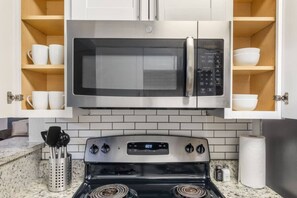 Una cocina con microondas de acero inoxidable, estufa y repisas de madera sobre la estufa.
