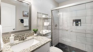 A bathroom with a granite countertop sink, a mirror, a shower with a glass door, and a shelf with toiletries.