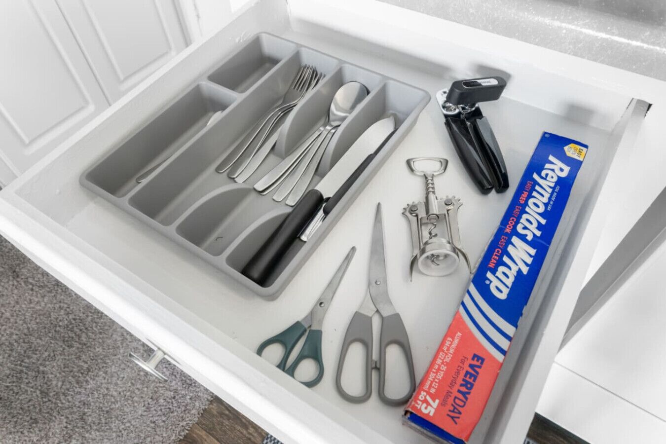 A drawer containing various utensils, a pair of scissors, and a cleaning product.