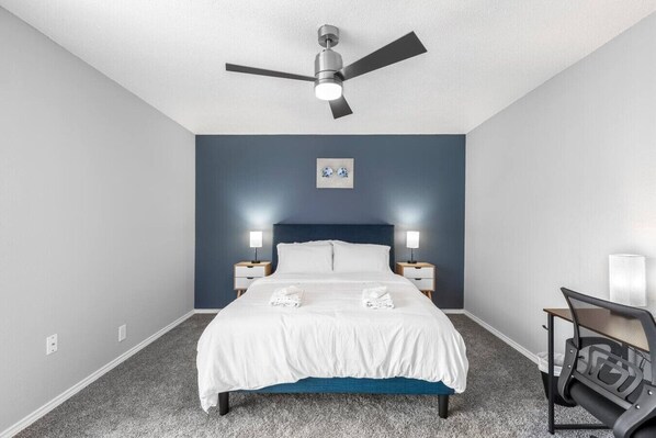 Une chambre à coucher avec un lit, deux tables de chevet avec des lampes, un ventilateur de plafond et une chaise.
