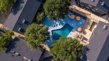 An aerial view of a residential area with a swimming pool surrounded by trees and a patio area with umbrellas.