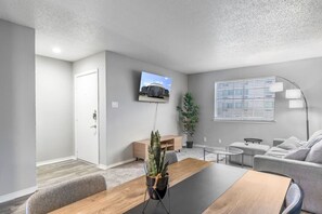 Un salon moderne avec un téléviseur à écran plat, une table basse en bois, un canapé gris et une plante en pot.