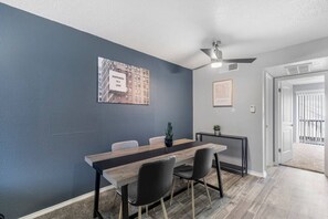 Un espace de salle à manger moderne, avec une longue table, des chaises et un ventilateur de plafond.