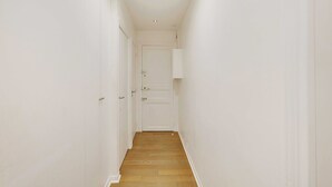 A narrow, white-walled hallway with wooden flooring leading to a closed door. - Beautiful Apartment 2br/6p - Eiffel Tower (Paris)