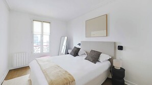 A bedroom with a large bed, a bedside table, a mirror, and a window. - Beautiful Apartment 2br/6p - Eiffel Tower (Paris)