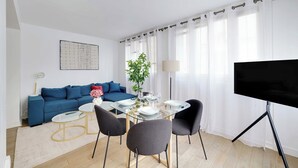 A modern living room with a blue sofa, a glass dining table, and a flat-screen TV. - Beautiful Apartment 2br/6p - Eiffel Tower (Paris)