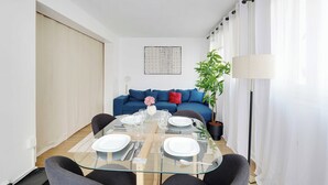 A modern living room with a glass dining table set for four, a blue sofa, a potted plant, and a floor lamp. - Beautiful Apartment 2br/6p - Eiffel Tower (Paris)