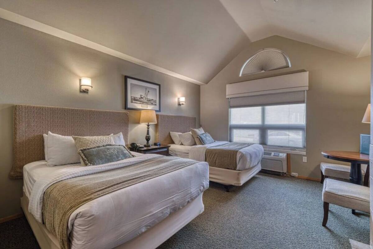 A hotel room with two beds, a desk, and a window with blinds.